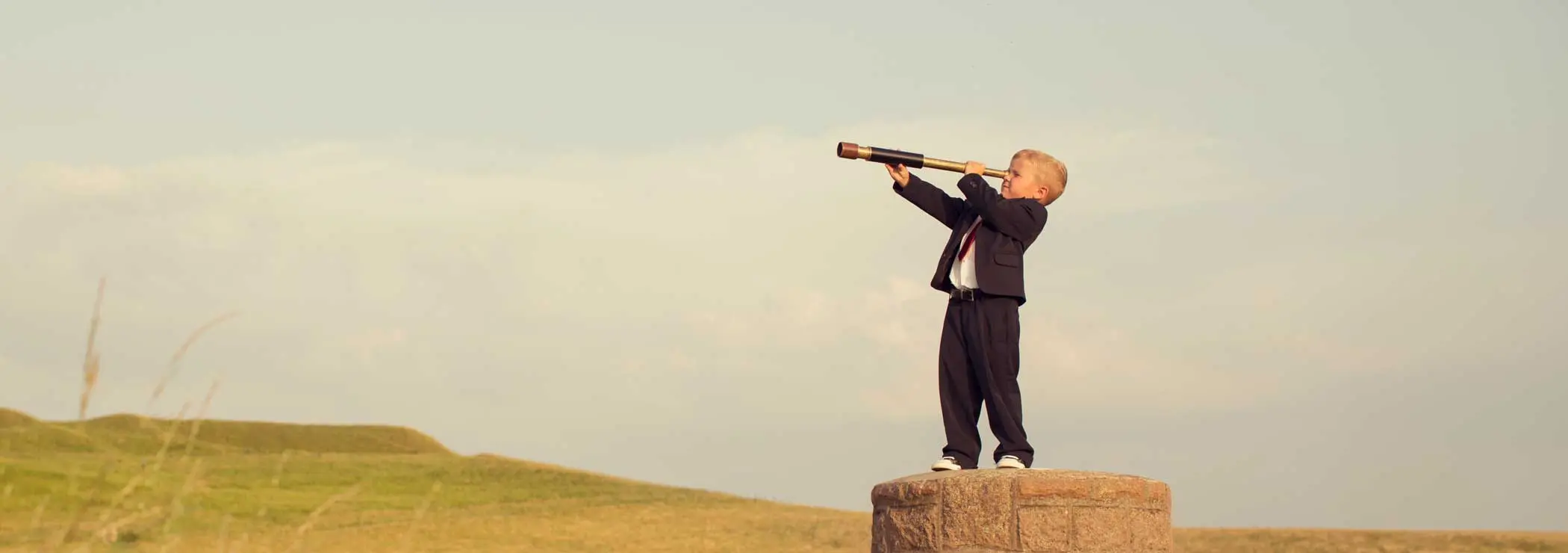Ein Junge steht auf einem Steinturm und schaut durch ein Fernrohr