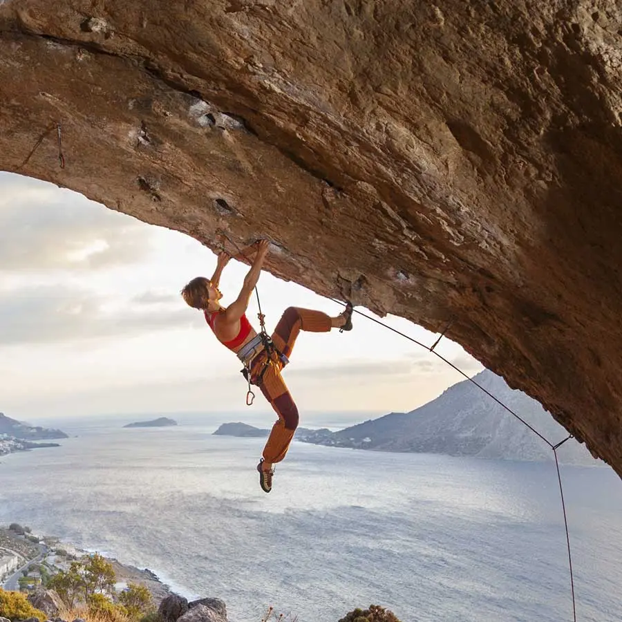 Woman climbs an overhang with a view of the sea