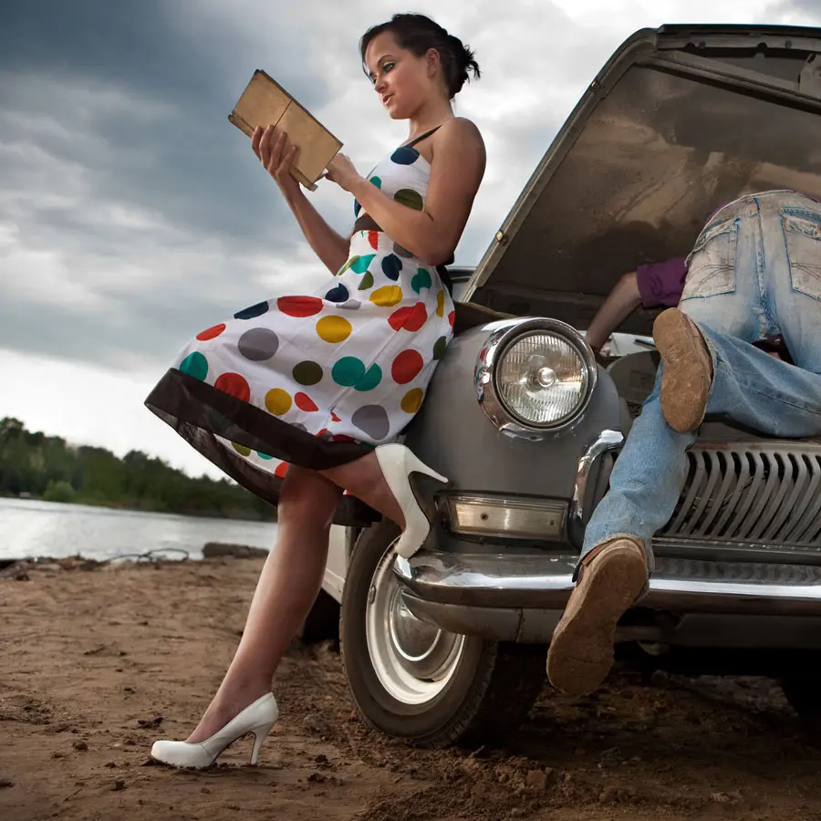 Woman reading a book while man tries to repair the car