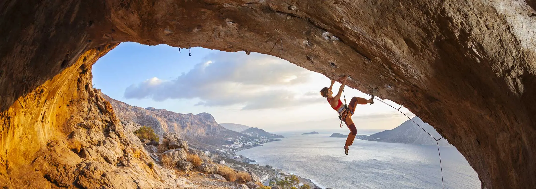Woman climbs an overhang with a view of the sea