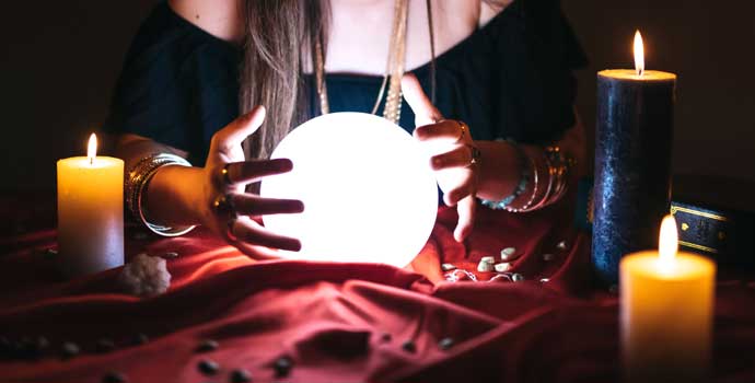 A fortune teller holds hands around a crystal ball