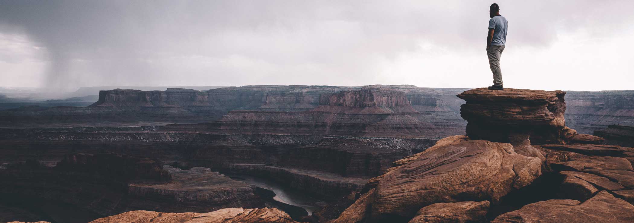 A man stands on the edge of a canyon on a flat rock