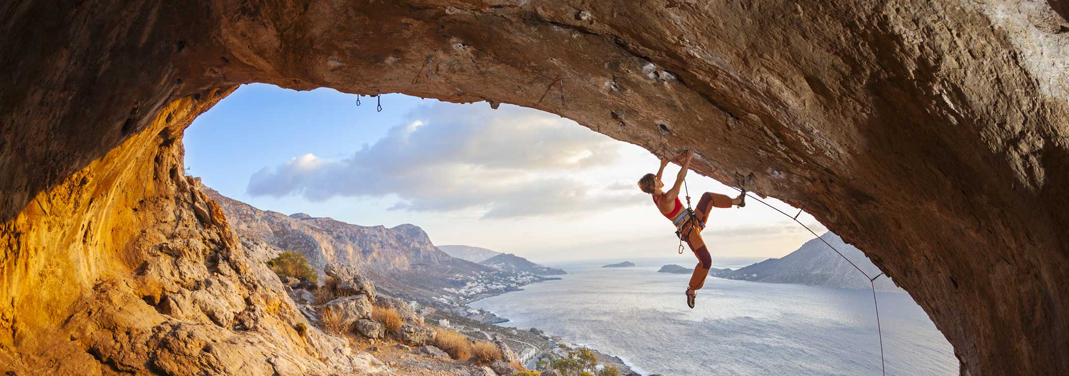 Woman climbs an overhang with a view of the sea