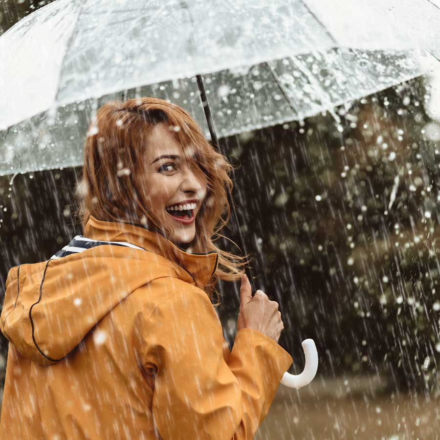 Eine fröhliche Frau mit Schirm schaut über ihre Schulter